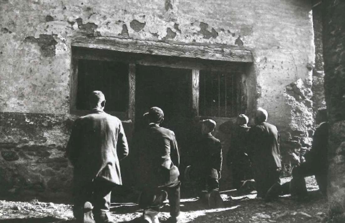 Sis veïns de Sornàs resen de genolls a terra davant l’església de Sant Roc: era també festa major (1930).