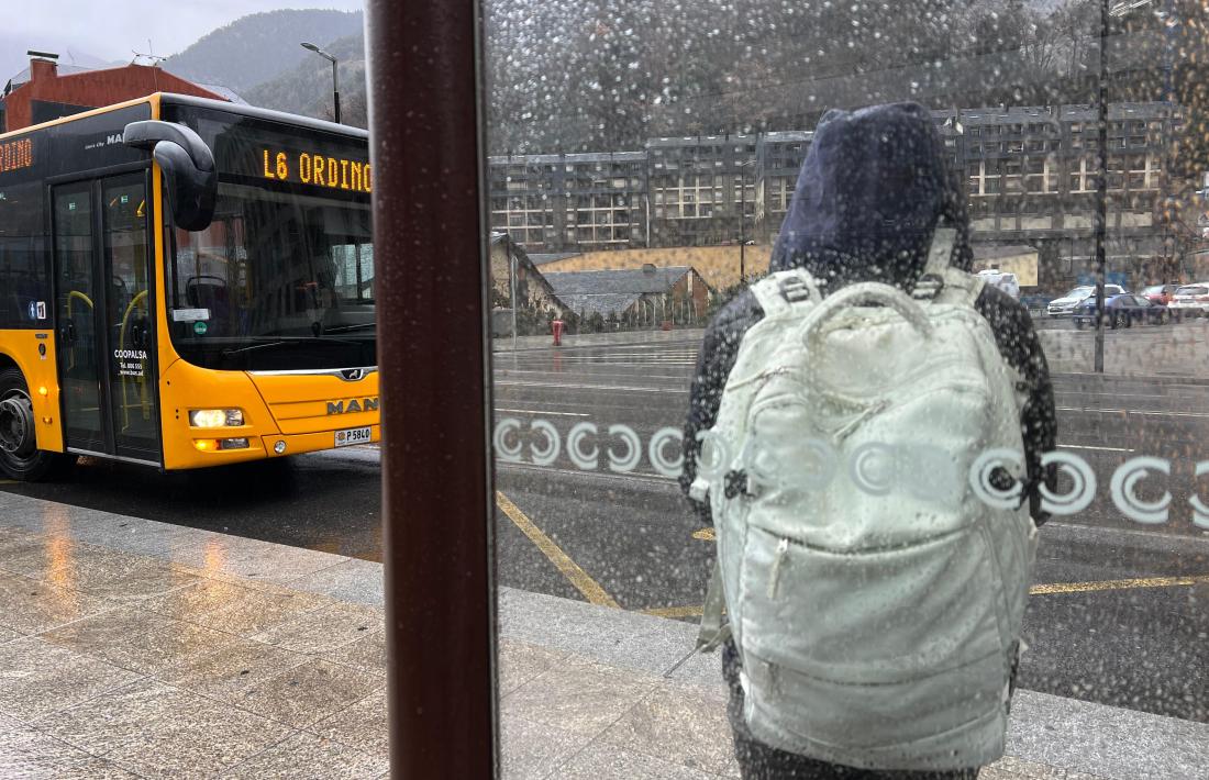 Un usuari del bus espera en una parada en un dia de pluja.