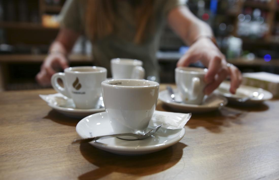 Una cambrera prepara cafès en una barra d’un bar.